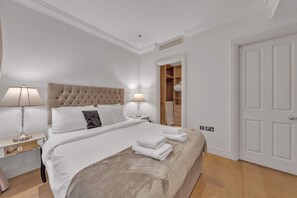 Ein Schlafzimmer mit einem großen Bett, zwei Nachttischlampen, einem Holz-Kopfteil, einem Kleiderschrank mit Spiegel und einer weißen Tür.
