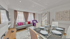 Ein modernes Wohnzimmer mit einer Couch, einem Esstisch für vier Personen und einer Treppe, die in eine andere Ebene führt.