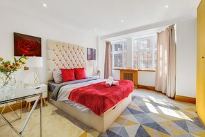 Ein Hotelzimmer mit einem großen Bett, einem Glastisch, einem Nachttisch, einem Fenster mit Vorhängen und einem Heizkörper.