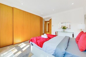 Ein Schlafzimmer mit einem Bett, einem Kleiderschrank, einem Nachttisch mit Lampe und einem Spiegel an der Wand.