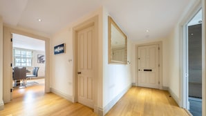 A hallway with wooden flooring, white doors, and a large mirror. - Luxurious 2 Bedroom in Mayfair (London)