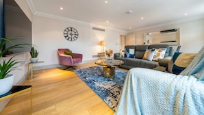 A modern living room with a sofa, armchair, coffee table, and a large clock on the wall. - Luxurious 2 Bedroom in Mayfair (London)