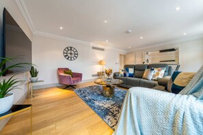 A modern living room with a sofa, armchair, coffee table, and a large clock on the wall. - Luxurious 2 Bedroom in Mayfair (London)