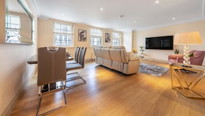 A spacious living area with a sofa, a dining table with chairs, a television, and a lamp. - Luxurious 2 Bedroom in Mayfair (London)