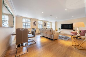 A spacious living area with a sofa, a dining table with chairs, a television, and a lamp. - Luxurious 2 Bedroom in Mayfair (London)