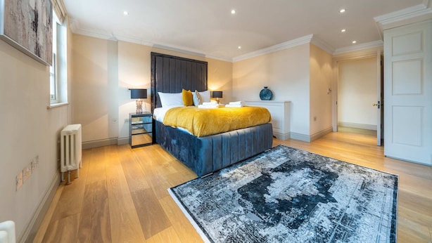 A bedroom with a bed, bedside tables, a radiator, a rug, and a door. - Luxurious 2 Bedroom in Mayfair (London)