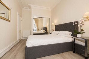 Ein modernes Schlafzimmer mit einem großen Bett, Nachttischen, einem Spiegel und Blick ins Freie.