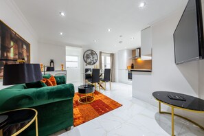 A modern living room with a green sofa, a dining area, and a kitchen. - Deluxe 1 Bedroom Apartment (London)