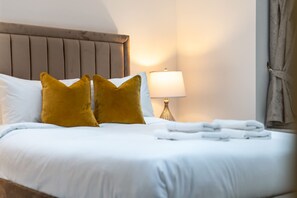 A neatly made bed with white linens, two mustard-colored pillows, and a bedside lamp. - Deluxe 1 Bedroom Apartment (London)
