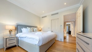 A bedroom with a bed, bedside tables, a dresser, and a hallway leading to another room. - Royal Two Bedroom Apartment (London)