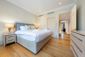 A bedroom with a bed, bedside tables, a dresser, and a hallway leading to another room. - Royal Two Bedroom Apartment (London)