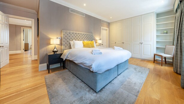 A bedroom with a large bed, bedside tables, a wardrobe, and a chair. - Royal Two Bedroom Apartment (London)