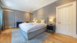 A modern bedroom with a large bed, bedside lamps, a wardrobe, and a door. - Royal Two Bedroom Apartment (London)