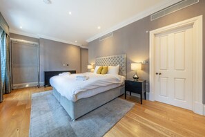 A modern bedroom with a large bed, bedside lamps, a wardrobe, and a door. - Royal Two Bedroom Apartment (London)