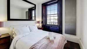 A hotel room with a large bed, a nightstand, a mirror, a window with a view, and a wall-mounted TV. - Superior One Bedroom Apartment in Belgravia (London)