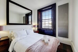 Ein Hotelzimmer mit einem großen Bett, einem Nachttisch, einem Spiegel, einem Fenster mit Blick und einem am Wand befestigten Fernseher.