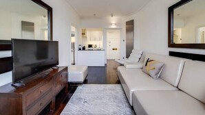 A modern living room with a flat-screen TV, a sofa, a coffee table, and a kitchen in the background. - Superior One Bedroom Apartment in Belgravia (London)