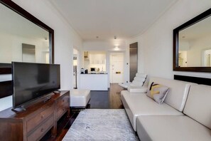 Ein modernes Wohnzimmer mit Flachbildfernseher, einer Couch, einem Couchtisch und einer Küche im Hintergrund.
