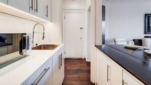 A narrow kitchen with white cabinets, a dark countertop, and a wooden floor. - Superior One Bedroom Apartment in Belgravia (London)
