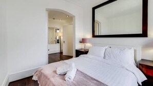 A hotel room with a bed, a nightstand, a lamp, and a large mirror on the wall. - Superior One Bedroom Apartment in Belgravia (London)
