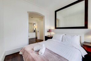 A hotel room with a bed, a nightstand, a lamp, and a large mirror on the wall.