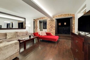 A living room with a beige sofa, a red sofa, a coffee table, a TV, and a brick wall. - Amazing 2 Bedroom Apartment in Belgravia (London)