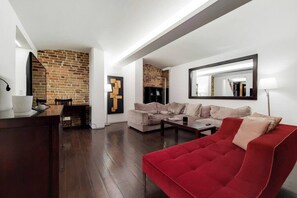 A modern living room with a red sofa, a brick wall, and a large mirror. - Amazing 2 Bedroom Apartment in Belgravia (London)