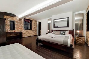 A bedroom with a large bed, a brick wall, and a modern ceiling design. - Amazing 2 Bedroom Apartment in Belgravia (London)