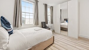 Ein modernes Schlafzimmer mit einem großen Bett, einem Sessel, einem Kleiderschrank und einem Spiegel.