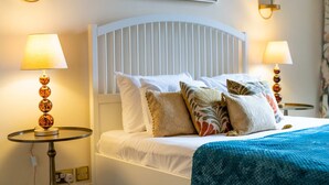 A neatly made bed with a white headboard, multiple pillows, and a blue blanket. There are two bedside lamps with round bases and a wall-mounted light fixture above the bed. - Deluxe 2 Bedroom Apartment In An Amazing Location (London)
