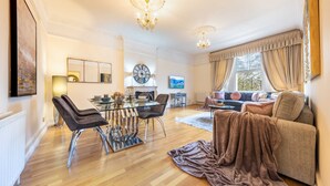 A spacious living room with a dining area, a large window with curtains, and a chandelier. - Deluxe 2 Bedroom Apartment In An Amazing Location (London)