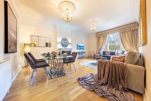 A spacious living room with a dining area, a large window with curtains, and a chandelier. - Deluxe 2 Bedroom Apartment In An Amazing Location (London)