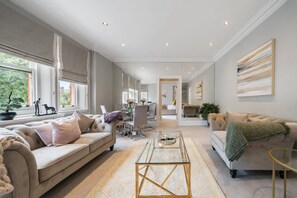 A spacious living area with a sofa, coffee table, and a dining area in the background. - Chic Spacious 2 Bedroom Duplex (London)