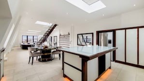 Eine moderne Küche mit einer zentralen Kochinsel, ein Essbereich mit einem runden Tisch und eine Treppe, die zu einer oberen Ebene führt.