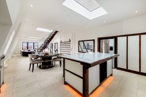 Eine moderne Küche mit einer zentralen Kochinsel, ein Essbereich mit einem runden Tisch und eine Treppe, die zu einer oberen Ebene führt.