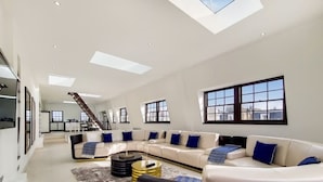 Ein geräumiges Wohnzimmer mit einem weißen Modulsofa, einem Couchtisch und einer Treppe, die in einen oberen Bereich führt.