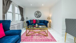 A modern living room with a blue sofa, a glass coffee table, and a grey armchair. - Cozy Haven Suite in London (London)