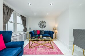 A modern living room with a blue sofa, a glass coffee table, and a grey armchair. - Cozy Haven Suite in London (London)