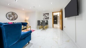 A modern living room with a blue sofa, a flat-screen TV, and a dining area with a table and chairs. - Cozy Haven Suite in London (London)