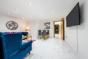 A modern living room with a blue sofa, a flat-screen TV, and a dining area with a table and chairs. - Cozy Haven Suite in London (London)