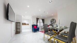 A modern dining area with a glass table, multiple chairs, and a television mounted on the wall. - Cozy Haven Suite in London (London)