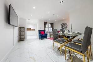 A modern dining area with a glass table, multiple chairs, and a television mounted on the wall. - Cozy Haven Suite in London (London)