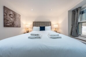 A hotel room with a large bed, two bedside lamps, a wall-mounted artwork, and a window with curtains. - Cozy Haven Suite in London (London)