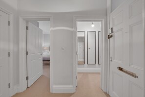 Um corredor com portas brancas, uma cama e um espelho.