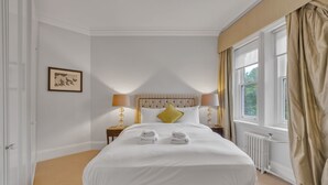 Ein Hotelzimmer mit einem großen Bett, zwei Nachttischlampen, einem gerahmten Bild an der Wand und einem Fenster mit Vorhängen.