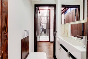 A narrow hallway with a wooden door, a white sink, and a mirror. - Magnificent 2 Bedroom Apartment In Belgravia (London)