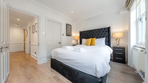 A hotel room with a large bed, bedside lamps, a nightstand, and a view of the hallway. - Super Deluxe 2bedroom Apartment in Mayfair (London)