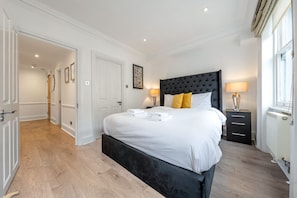 A hotel room with a large bed, bedside lamps, a nightstand, and a view of the hallway. - Super Deluxe 2bedroom Apartment in Mayfair (London)