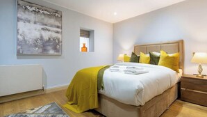 A bedroom with a bed, bedside lamps, a painting, and a radiator. - Sophisticated Splendor2-bedroom House in Mayfair (London)