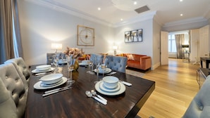A dining area with a dark wooden table set for six, flanked by two sofas, one with a tufted backrest and the other with a plush, orange fabric. - Royal 4 Bedroom Apartment (London)